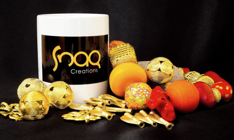 Snaq Creations branded mug surrounded by handcrafted gold, orange and red beads